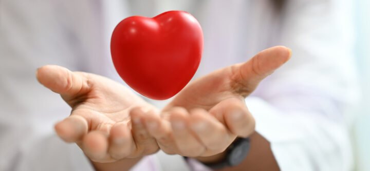 Red heart floating over opened hands. Health care, cardiological, medical and charity concept.